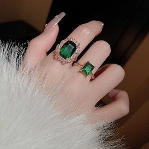Detail of emerald green gemstone rings set in gold finish worn on model hand