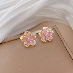 Close-up of gold flower earrings with pink gems and crystals in a beige jewelry box