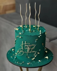 Detail of green frosted cake with gold Happy Birthday acrylic topper and five candles