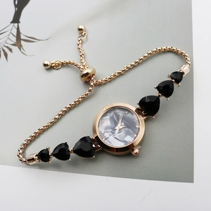 Detail of golden watch with black marble dial and heart-shaped charms on bracelet