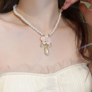 Close-up of pearl necklace with pink rose flowers, bow and teardrop pearl pendant