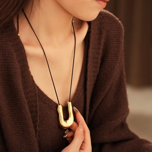 Gros plan d'un collier doré en forme de U avec cordon noir porté par un mannequin