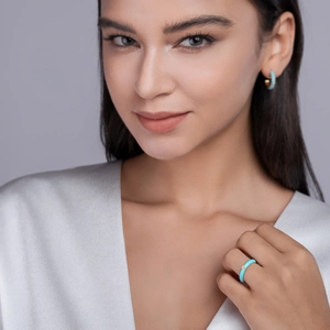 Detailed view of light blue enamel ring and earrings set on model with silver silk outfit