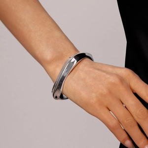 Close-up of a minimalist silver wavy irregular open bangle with a high-polished mirror finish