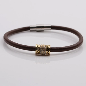Dettaglio del bracciale in pelle marrone con perla dorata e zirconi e chiusura magnetica
