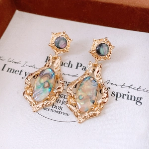 Detailed close-up of shell pendant earring with golden frame and iridescent blue shell inlay