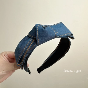 Close-up of a blue denim headband with large bow detail held against a plain background