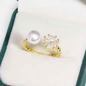 Detailed close-up of a golden twist ring with pearl and clover-shaped heart zircons
