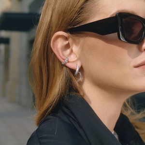 Detail of silver twisted earrings and zircon ear cuff worn by a model in close-up view