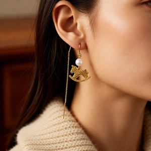 Close-up of golden rocking horse earring with a pearl on a model's ear