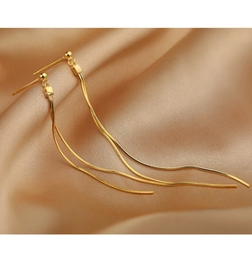Detail of long gold tassel earrings with sleek snake chains on champagne satin