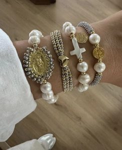 Détail de bracelets en perles superposés avec breloques Vierge Marie et croix en or