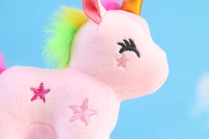 Dettaglio ravvicinato di unicorno di peluche rosa con corno dorato e criniera arcobaleno