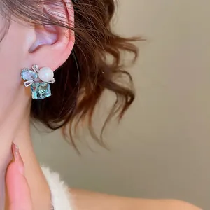 Bow pearl stud earrings with light blue square gemstone on model ear for elegant style