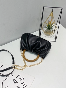 Detail view of black pleated cloud bag with round wooden handle and gold chain strap