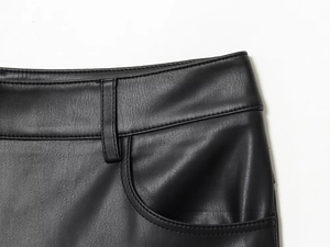 Detail view of black faux leather trousers with belt loops and stitching