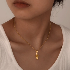 Minimalist gold cross pendant necklace with fine chain on woman wearing knitwear