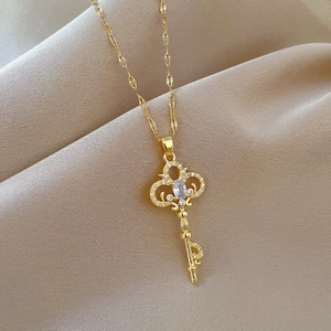 Close-up of golden key pendant necklace with sparkling crystals on beige fabric