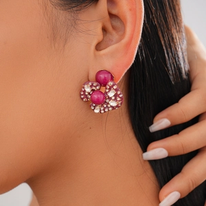 Close-up of elegant gold earrings with magenta resin stones and white rhinestones on model