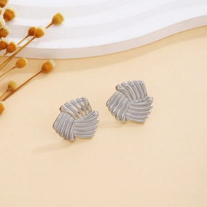 Detail shot of silver fan-shaped twisted knot stud earrings on a beige surface