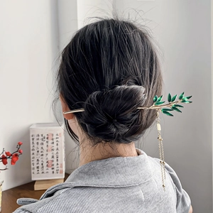 Elegant gold bamboo tassel hair stick with green leaves worn on a classic updo bun