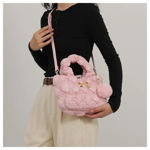Pink quilted shoulder bag with gold bow detail and fluffy pompom charm on model