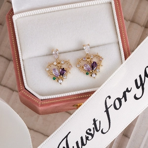 Detailed shot of golden heart earrings with purple zircons and pearls in a pink velvet box
