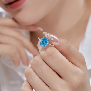 Close-up of a square-cut blue sapphire ring with sparkling zircon halo on hand