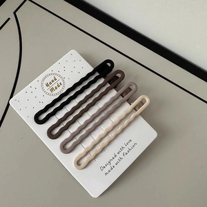 Detail of four matte wave hair clips in earth tones displayed on a handmade card