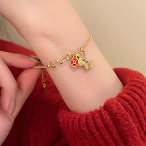 Detail of red cord bracelet with gold zodiac dog and coin pendants on a red sweater