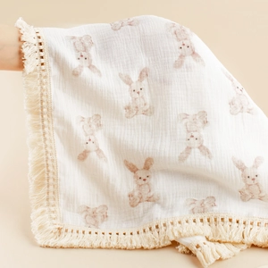 Detailed texture of cotton gauze baby blanket with rabbit print and cream tassel trim