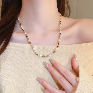 Detail of freshwater pearl and brown agate beaded necklace on beige knitwear model