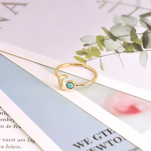 Detail of gold moon and turquoise bead on adjustable open ring atop a magazine