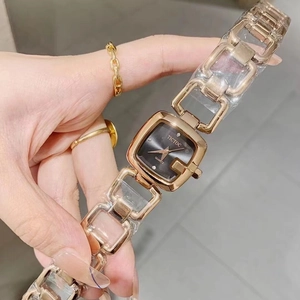 Close-up of golden square watch with black dial and chain strap on female wrist