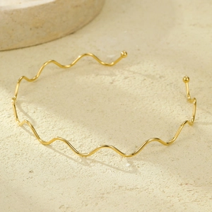Detail of 18K gold-plated wavy stainless steel necklace on a textured stone surface