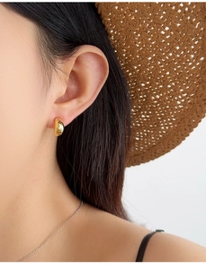 Close-up of minimalist gold-plated C-shaped curved earrings on a model with a straw hat