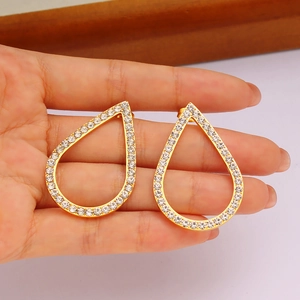 Detailed view of hand holding gold teardrop earrings with white zircon crystal inlay