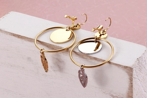 Detail view of two-tone gold and silver earrings with leaf pendant on a stone base