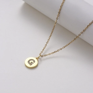 Detail of gold chain necklace featuring a circular pendant with zircon-inlaid letter G
