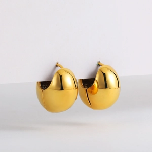 Close-up of chunky gold dome earrings with a high-polished mirror finish on a white stand