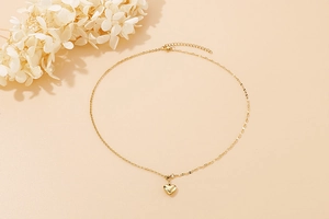 Flat lay of a delicate golden heart pendant necklace on a clean beige background