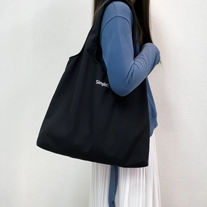Détail d'un grand cabas en toile noire avec lettrage Simplicity porté par un mannequin
