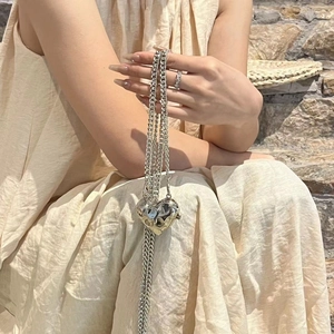 Silver liquid metal heart pendant long chain necklace shown by a model on stone steps