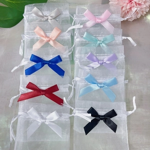Assorted colorful organza gift bags with satin drawstring bows on a soft fabric surface