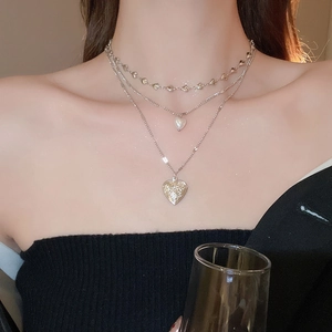 Close-up of triple-layered pearl necklace with vintage floral heart pendant on model