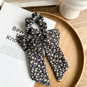 Detailed view of black floral scrunchie with long ribbon bow on aesthetic wood tray