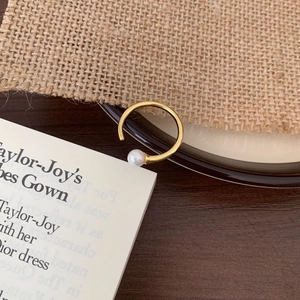 Detail of minimalist gold C-shaped sterling silver ring with white round pearl on wood