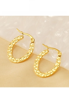 Macro view of gold plated oval hoop earrings featuring a hammered texture and pin closure