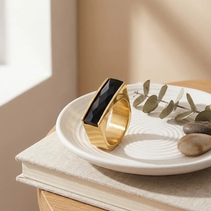 Close-up of a wide gold stainless steel ring with black faceted gemstone on a white tray