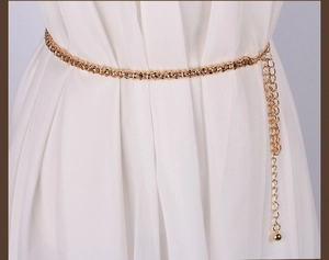 Detail of gold metal link chain belt with ball pendant styled on a white dress